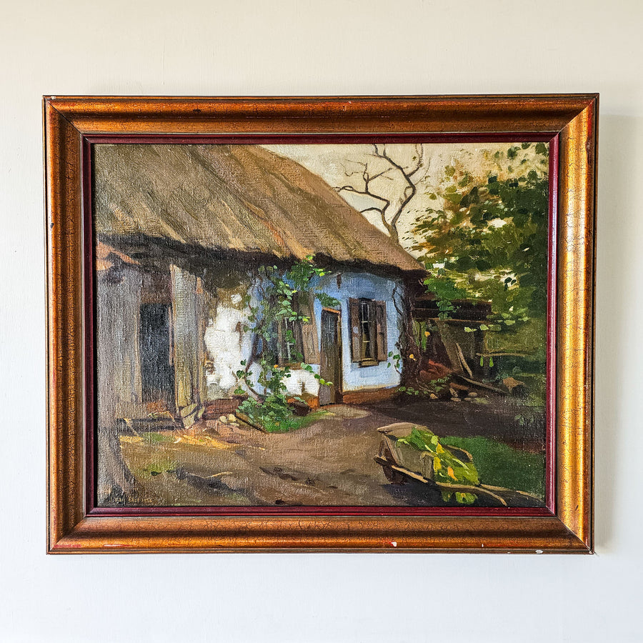 1938 vintage Dutch oil painting signed by J. Van Elst, featuring a quaint thatched cottage amidst lush greenery with a wheelbarrow filled with crops, framed in textured golden-brown wood.