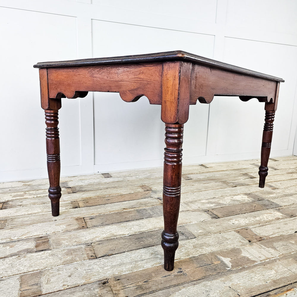 an Early 20th Century ecclesiastical-style pitch pine table with slim legs and a shaped apron. Ideal for dining rooms, living rooms, or studies, this antique pine table adds tasteful charm to any space, blending seamlessly with various décor styles for a warm and character-filled home.