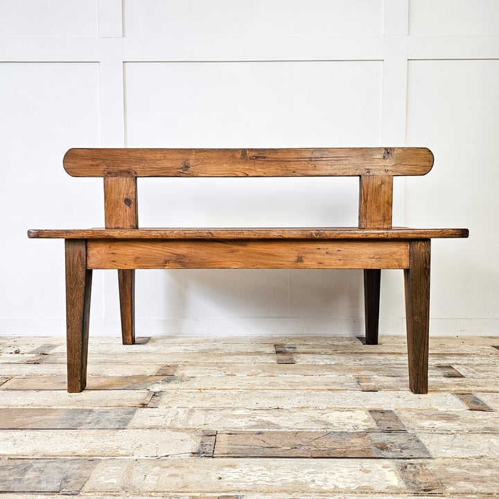 An antique Early 20th Century Pitch Pine Station Bench showcasing a rectangular seat with central backrest, worn patina, and straight legs - a piece of history and vintage charm for any interior.