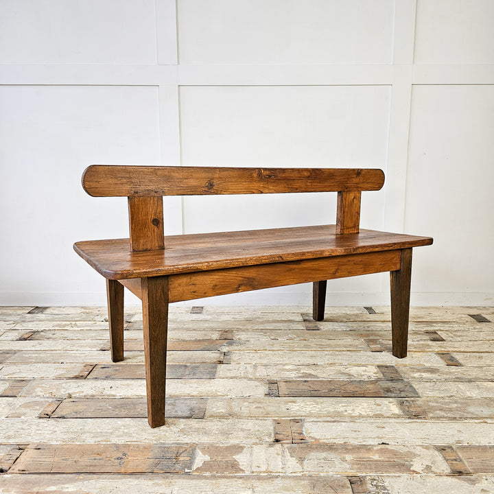 An antique Early 20th Century Pitch Pine Station Bench showcasing a rectangular seat with central backrest, worn patina, and straight legs - a piece of history and vintage charm for any interior.