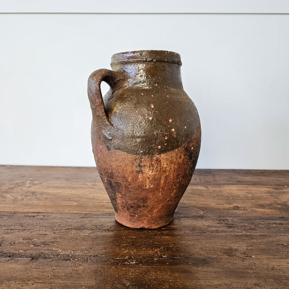 An angled view of an antique glazed turkish vessel showing the rustic texture of the terracotta and the rustic green glaze