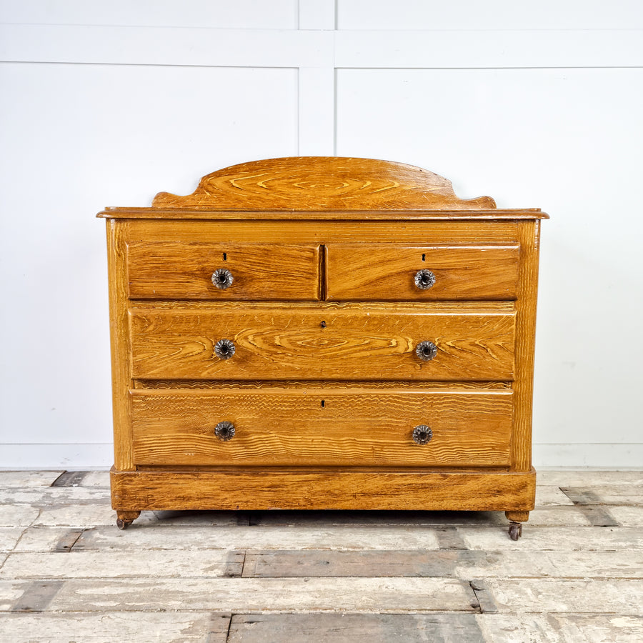 A 19th Century Pine Chest of Drawers with Original Scumble Glaze. The chest features a shaped upstand above a rectangular moulded top and has two short drawers over two long drawers with decorative glass knobs. It is raised on four castors for easy manoeuvrability.
