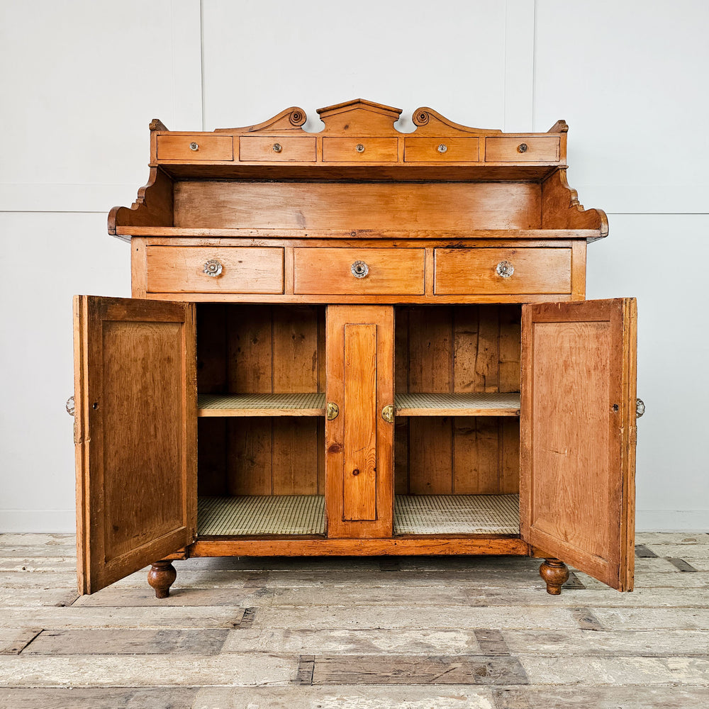 Front View: An antique pine dresser or sideboard with it's cupboard doors open showcasing the interior shelves lined with vinyl.