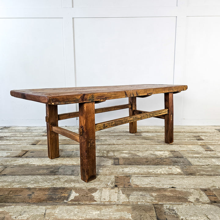 A vintage elm coffee table with a weathered top showcasing natural wood beauty. Sturdy straight legs and lower stretchers provide durability. Warm waxed patina adds richness