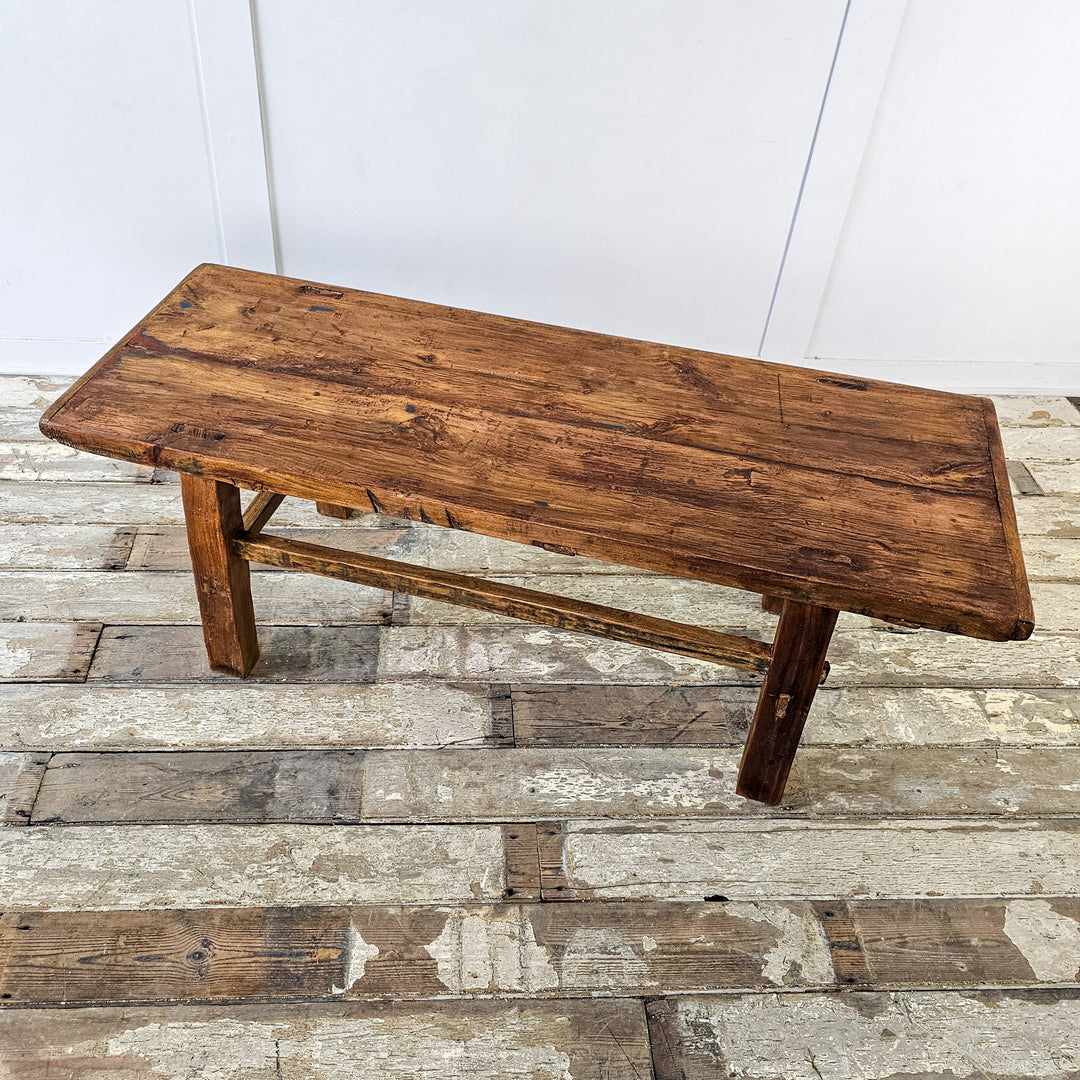 A vintage elm coffee table with a weathered top showcasing natural wood beauty. Sturdy straight legs and lower stretchers provide durability. Warm waxed patina adds richness