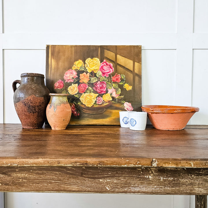 A staged view of Violet Harrison's vintage floral oil painting placed on a wooden surface, flanked by rustic earthenware pots, creating a charming and artistic display.