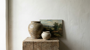 A curated group of antique studio pottery and an original oil painting, set against a minimalist textured plaster wall.
