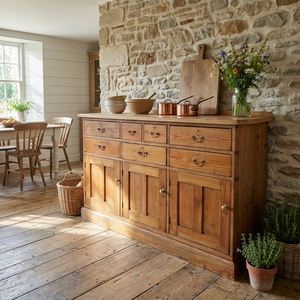 A large 19th-century country house style kitchen dresser base in rustic pine with seven drawers, three cupboards and matching brass handles. The lighter scrubbed top with cleated ends contrasts with the deeper base, creating a practical sideboard for organised household storage.
