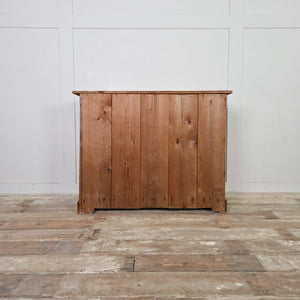 A farmhouse-style antique pine chest of drawers with four drawers arranged two over two. The chest has Art Nouveau–style brass handles, simple mouldings and a warm red-stained wax finish. It stands on a sturdy plinth base typical of late 19th to early 20th century pine furniture.