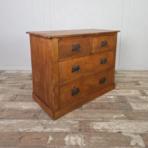 A rustic farmhouse-style antique pine chest of drawers finished in a warm red-stained wax. It features two short drawers over two full-width drawers, all with decorative Art Nouveau–style brass handles. The chest is framed with simple mouldings and set on a solid plinth base.