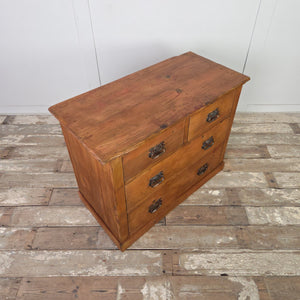 A farmhouse-style antique pine chest featuring four drawers in a two-over-two formation. The pine has a red-stained wax finish, and the decorative brass handles show curved Art Nouveau influence. The piece is built on a sturdy plinth base.