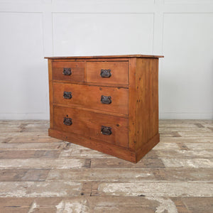 A rustic antique pine chest of drawers featuring a warm red-stained wax finish and a two-over-two drawer layout. Each drawer has a decorative Art Nouveau–style brass handle. The chest is supported by a plain plinth.