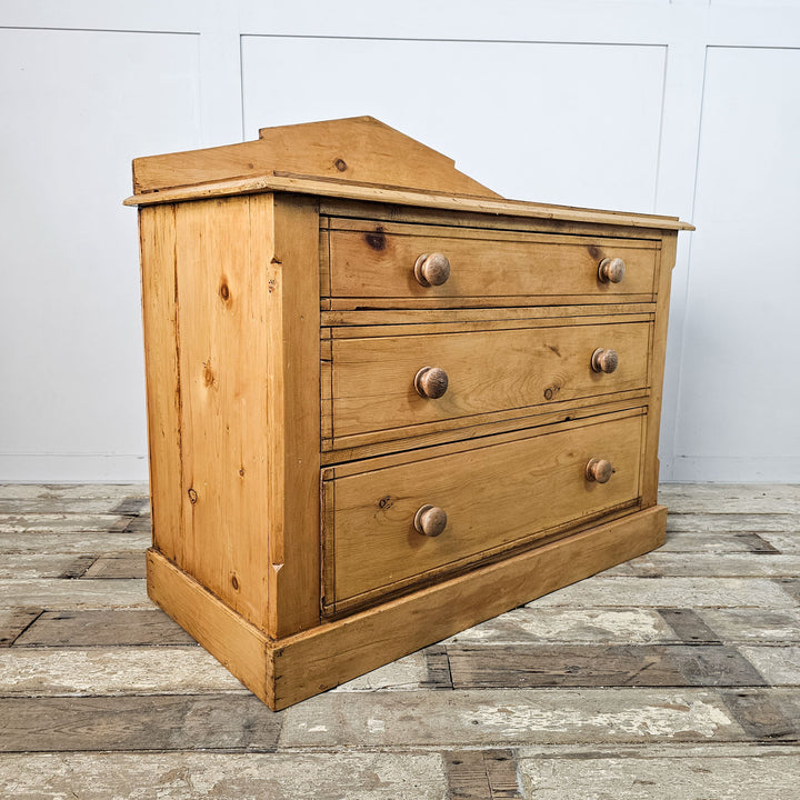 Angle perspective of an antique pine chest of drawers, displaying the texture of the wood and the classic round knobs.