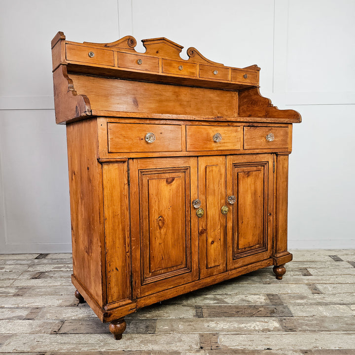 Angled View: Scottish Pine Dresser featuring a shaped gallery back with a series of small drawers above a further three drawers and two door cupboard. The angled view showcases the decorative shaped sides of the upper gallery. 