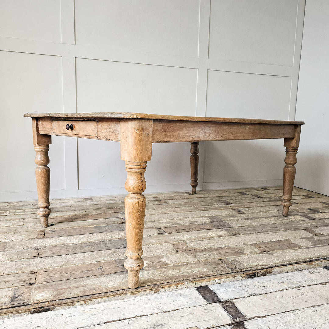 A side angled view of a large antique dining table in piine from the 19th century showing the turned legs.