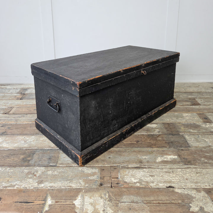 A Victorian pine storage chest with black painted exterior and colourful interior lining for visual contrast.
