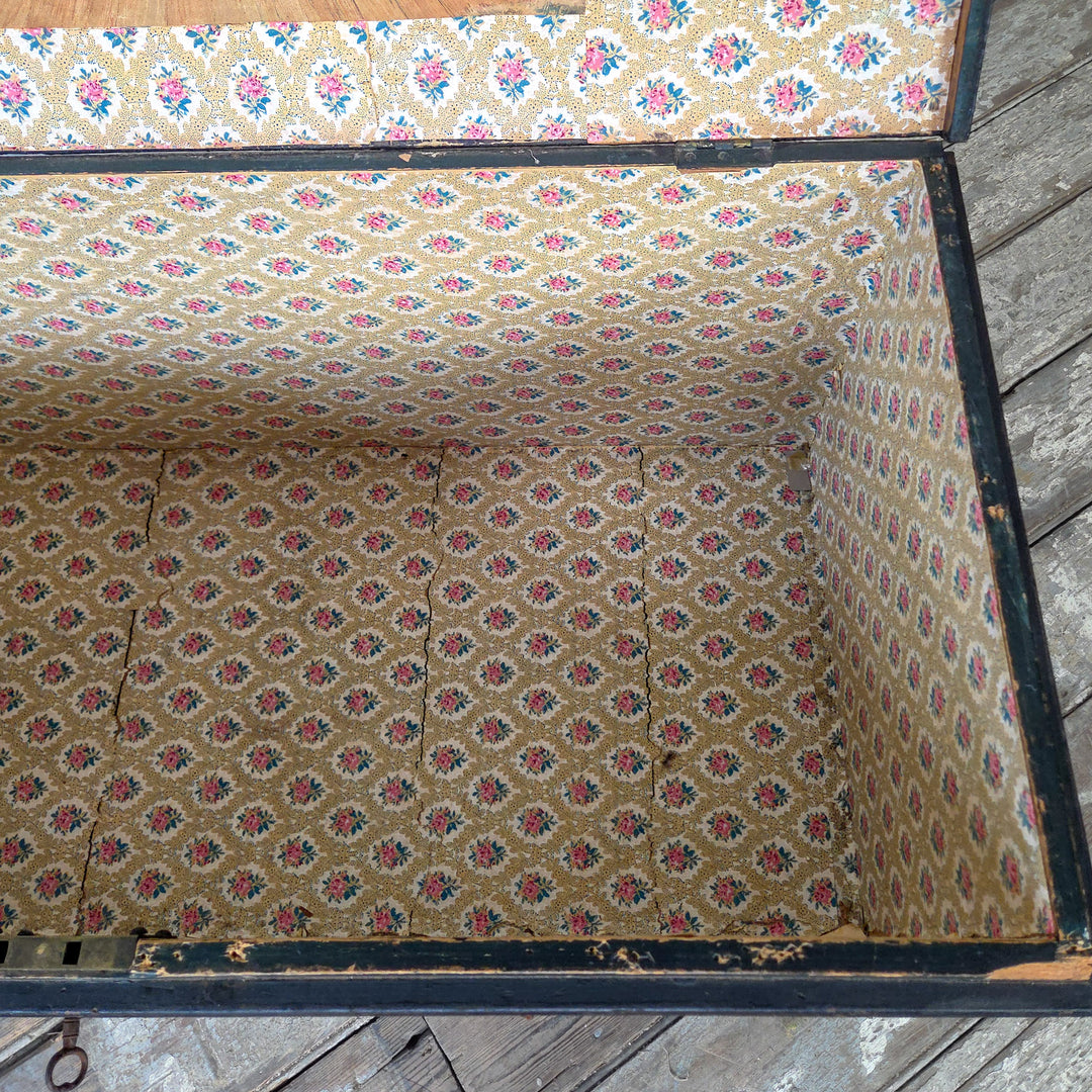 A painted pine trunk from the 19th century with hinged lid, paper-lined interior and metal side handles.
