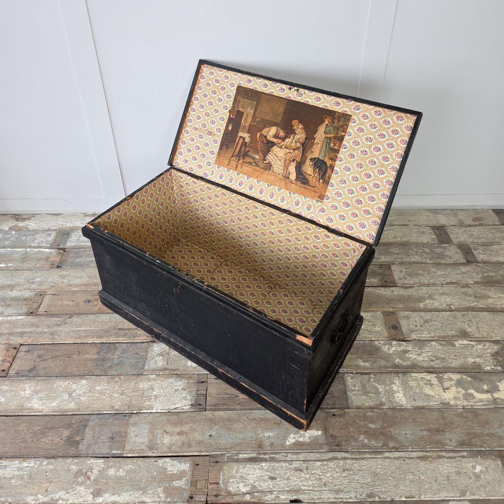 An antique pine storage chest with decorative paper-lined interior and hinged lid for practical storage.

