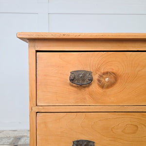 A waxed pine chest of drawers with three graduating drawers, antique early 20th century in origin, featuring decorative swing handles, plinth base, and honey pine tones, a versatile piece of farmhouse storage furniture suitable for use as bedroom drawers or a rustic storage chest.