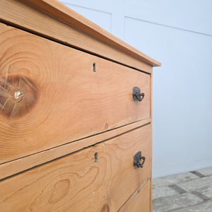 Antique pine chest from the early 20th century with three drawers, fitted with contrasting dark metal swing handles, raised on a plinth base, with a wax finish enhancing the natural grain, perfect as farmhouse bedroom drawers, cottage storage drawers, or rustic pine furniture.