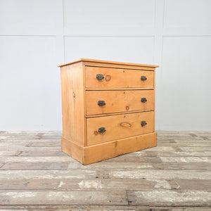 A solid pine chest of drawers dating to the early 20th century, offering three spacious drawers with decorative metal handles, a waxed finish to highlight the natural grain, and a sturdy plinth base, making it a practical storage chest or antique bedroom drawers for rustic interiors.
