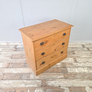 A rustic pine chest of drawers from the early 1900s with three graduating drawers, dark metal swing handles, and a plinth base, finished with furniture wax to protect the wood, perfect for use as antique bedroom drawers, farmhouse storage drawers, or a practical pine chest.