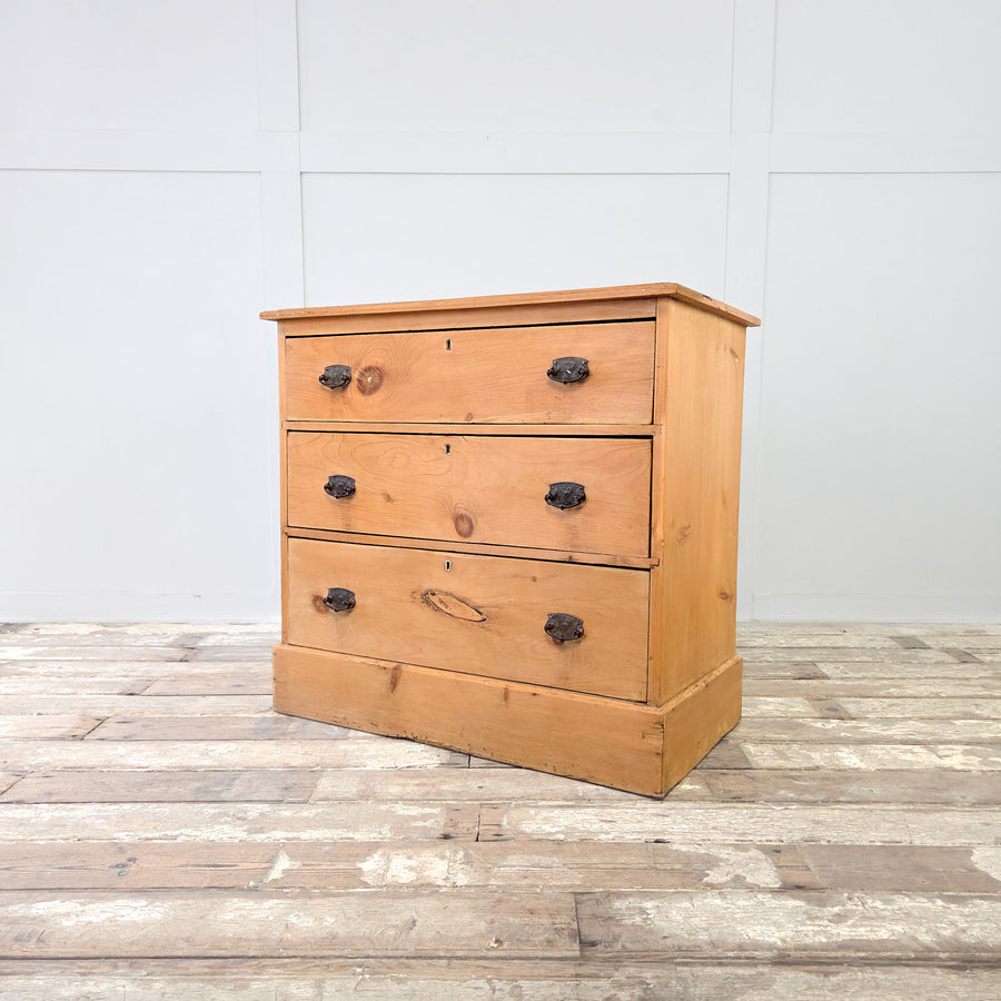 An early 20th century antique pine chest of drawers featuring three graduating drawers with original metal swing handles, raised on a plinth base, finished in honey-toned pine with a waxed surface, perfect as rustic farmhouse bedroom drawers or a versatile storage chest.