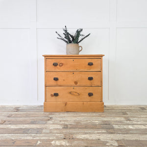 Antique pine storage chest from the early 1900s with three drawers of increasing depth, fitted with dark metal swing handles that contrast against the warm pine patina, ideal for use as farmhouse bedroom drawers, a country cottage storage piece, or rustic hallway furniture.