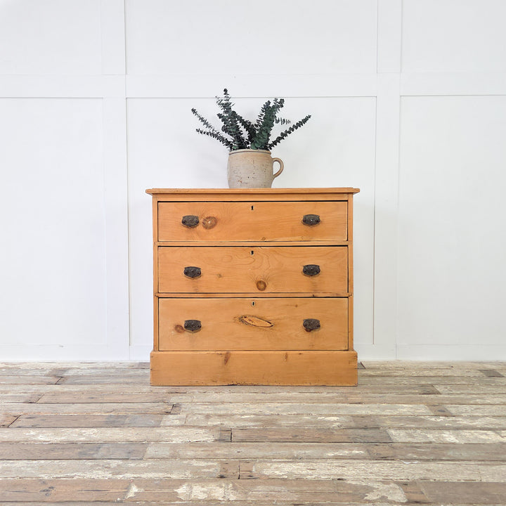 Antique pine storage chest from the early 1900s with three drawers of increasing depth, fitted with dark metal swing handles that contrast against the warm pine patina, ideal for use as farmhouse bedroom drawers, a country cottage storage piece, or rustic hallway furniture.