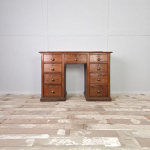 A rustic antique pine desk from the early 20th century featuring a central kneehole with nine drawers arranged to either side. The drawers graduate in depth and are fitted with original brass knob handles.
