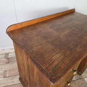 An early 20th century antique pine desk with nine storage drawers set around a central kneehole. The drawers graduate in depth from top to bottom and retain their original brass knob handles.
