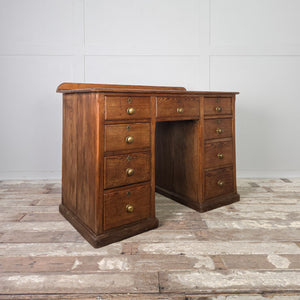 An early 20th century antique pine desk with a central kneehole flanked by nine drawers graduating in depth. The drawers retain their original brass knob handles, and the desk is constructed on a simple plinth base.
