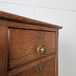 An antique pine desk from the early 20th century featuring a central kneehole flanked by nine graduated drawers. Original brass knob handles are fitted throughout, and the desk is raised on a simple plinth base.
