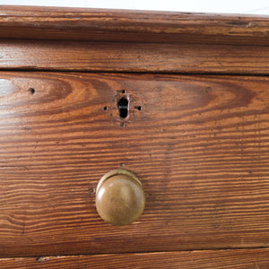 A rustic early 20th century antique pine desk with nine drawers arranged around a central kneehole. The drawers graduate in size and are fitted with original brass knobs.

