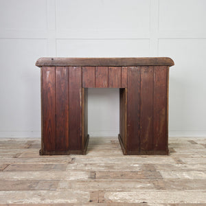 An antique pine kneehole desk dating from the early 20th century, with nine graduated drawers arranged around the kneehole opening. The desk retains its original brass knob handles and a straightforward plinth base.
