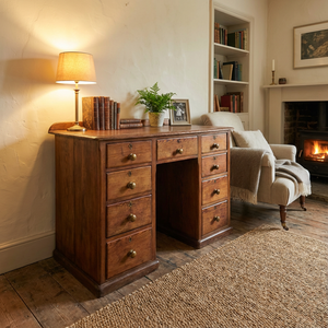 An antique pine kneehole desk from the early 20th century with nine graduated drawers set around a central kneehole. Each drawer is fitted with original brass knobs, and the desk stands on a simple plinth base.
