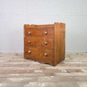 Antique ash three drawer chest with a gallery-style back, graduated drawer depths, simple round wooden knobs, and a shaped plinth base dating from the early 20th century.

