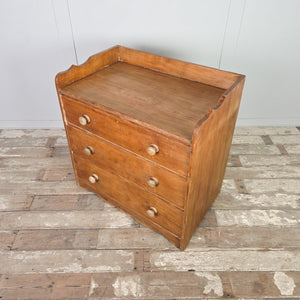 Antique ash chest of drawers from the early 20th century, showing three drawers that increase in depth from top to bottom, fitted with wooden knobs and a gallery back.
