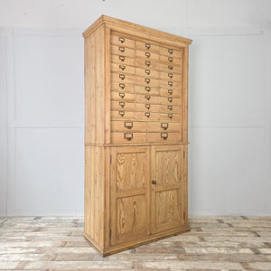 A large early 20th century pine storage cabinet with thirty-four small drawers in the upper section, a two-door cupboard below, and a neutral clear wax finish to protect the natural pine grain.