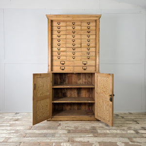 An early 20th-century antique pine storage unit featuring 34 drawers with brass label holders, set above a two-door cupboard with fixed shelves. The clear wax finish highlights the pine grain, giving this country-style bank of drawers practical, organised storage for home items.