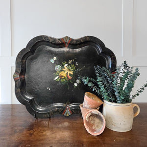 A mid to late 19th century Victorian papier-mâché serving tray with a black lacquered finish, scalloped edges with border detail, and a vibrant handpainted bouquet to the centre with mother of pearl inlay. Originally made for serving tea or drinks, it is now well suited to decorative display on a table, stand, or wall.