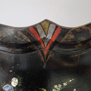 An antique Victorian papier-mâché serving tray dating from the mid to late 19th century, featuring a black lacquered surface, scalloped edge detailing, and a central floral design with mother of pearl inlay. A decorative piece that can be displayed on a tabletop or used as wall décor.