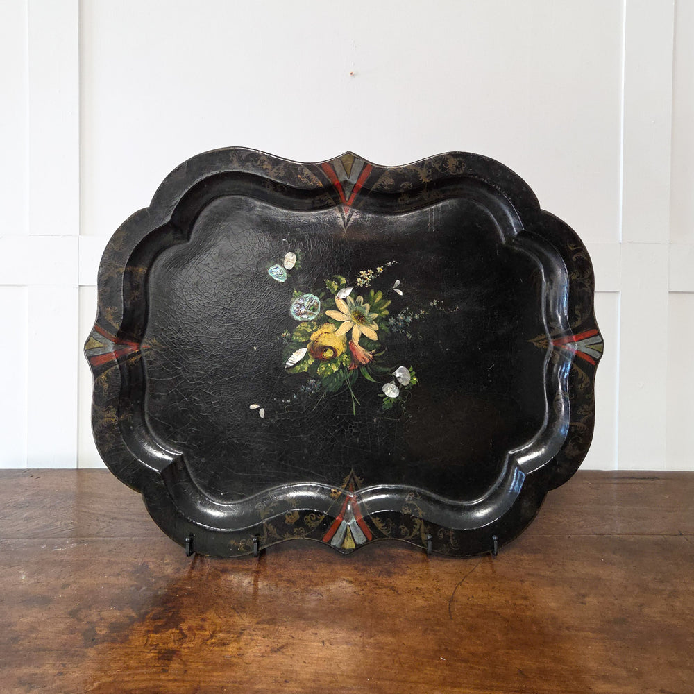 A large Victorian papier-mâché serving tray from the 19th century with a lacquered black background, hand-painted floral decoration, mother-of-pearl inlay and scalloped edge, perfect as a decorative centrepiece, wall-mounted tray or console display.