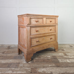 An early 19th-century pine and ash chest of drawers in a two-over-two layout with round wooden knobs and original ivory escutcheons. A simple farmhouse style piece with panelled sides and shaped bracket feet, providing useful storage around the home.