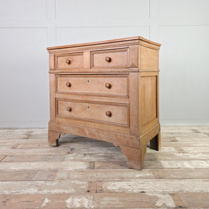A cottage style early 19th-century chest of drawers with a pine and ash frame, round wooden knobs and original ivory escutcheons. The two-over-two drawer layout and shaped bracket feet create a straightforward, functional storage chest.