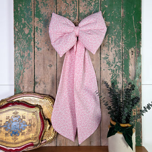 A large handmade fabric bow made in small batches from genuine vintage Laura Ashley “Firenze” cotton with a pink damask motif. Softly padded with sculpted form and finished with an antiqued brass hoop, offering a country or cottage-style decorative bow for doors, furniture or display.