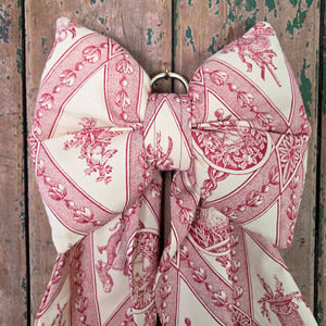 A handmade limited-edition bow crafted from genuine vintage fabric, featuring a padded and structured design with tapering tails. Finished with an antiqued brass ring for hanging, it’s ideal for adding a decorative country-house touch to doors, furniture, or mantels.