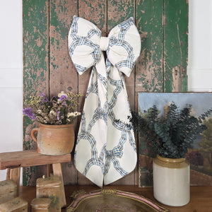 A handmade decorative fabric bow crafted from vintage Sanderson “Carousel” fabric, featuring padded construction, gently tapered tails and a removable brass hanging hoop. The vintage fabric gives the bow a traditional country character, with each piece made in small, unrepeatable batches.