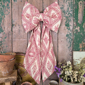 A handmade decorative fabric bow from the Country House collection, crafted from genuine vintage fabric and lightly padded for a full shape. Finished with an antiqued brass hanging hoop, this limited edition bow is perfect for styling on doors, mantels, or furniture.