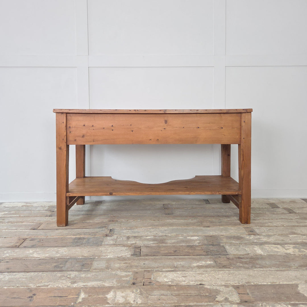 A Victorian pine farmhouse table from the 19th century with planked top, two drawers and lower shelf, raised on chunky legs. Originally used as a prep table, it is equally suited to life as a serving table, console or sideboard. This antique pine work table combines straightforward design with useful storage, making it a versatile Victorian piece for the kitchen, dining room or hallway in any farmhouse or rustic interior.